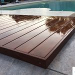 Gros plan d'un caillebotis en bois d'un volet immergé, avec un volet de piscine immergé en déploiement en arrière-plan, en plein jour.
