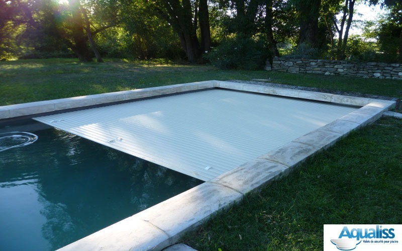 Volet de piscine immergé avec tablier de lames blanches, en train de se déployer dans une piscine à Avignon, photographié en journée.
