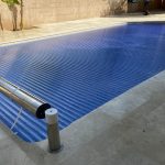 Volet de piscine hors sol avec tablier en polycarbonate bleu, en position fermée sur le bassin, en plein jour.