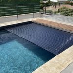 Volet de piscine immergé en polycarbonate se déployant sur l'eau d'une piscine durant une journée ensoleillée à Marseille.