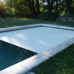 Volet de piscine immergé en train de se dérouler sur l'eau, capturé en pleine journée dans un jardin à Alès.