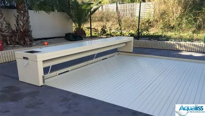 Volet de piscine en forme de banc, de couleur vanille, en position fermée sur une piscine à Marseille, photographié en journée.