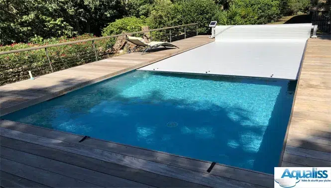 Volet de piscine mobile gris, en train de se dérouler sur une piscine à Arles, photographié en journée.