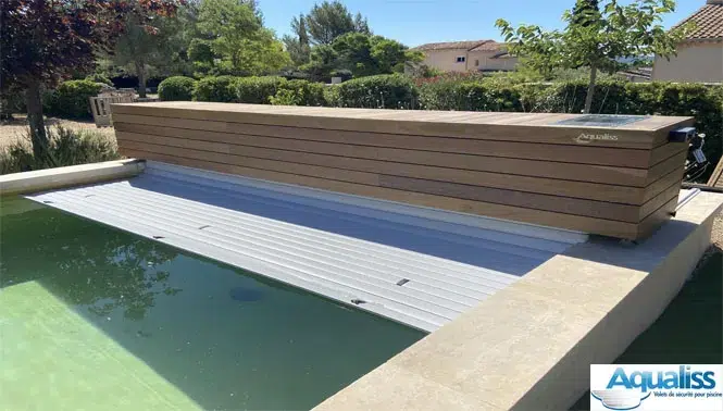 Volet de piscine sur rails avec coffre en bois, en train de se dérouler sur une piscine à Montpellier, photographié en journée.
