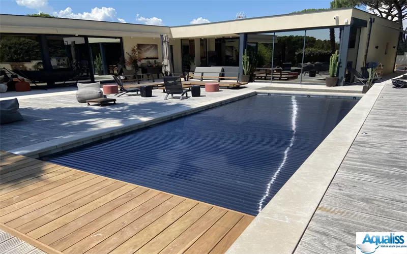 Couverture de piscine immergée avec lames en polycarbonate noir, en position fermée sur une piscine à Marseille, photographiée en journée.