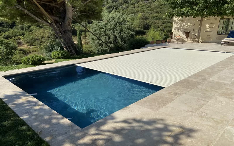 Volet de piscine plage immergée avec lames couleur vanille, se déroulant dans la piscine, photographié en plein jour à Arles.