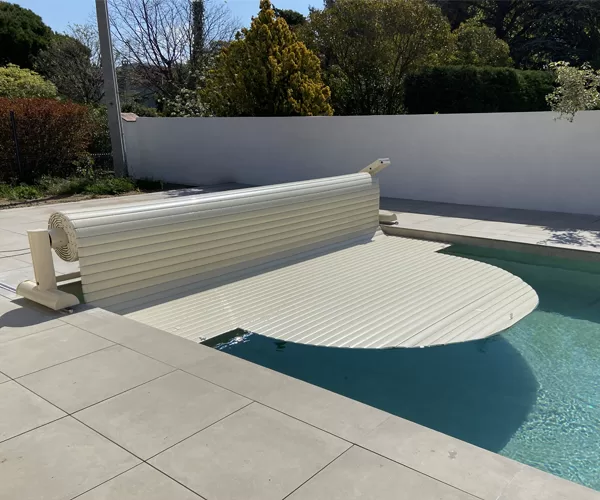 Volet de piscine mobile couleur vanille, se déroulant avec son tablier de lames sur la piscine, photographié en pleine journée à Arles.
