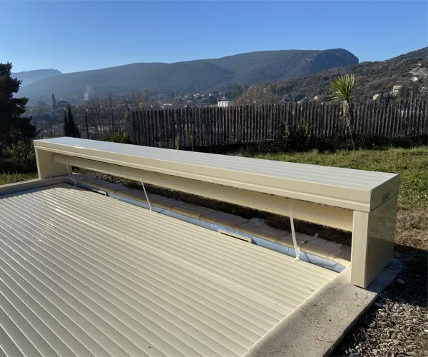 Volet de piscine hors sol en forme de banc de couleur sable, en position fermée sur la piscine, photographié en pleine journée avec un paysage en arrière-plan à Alès.