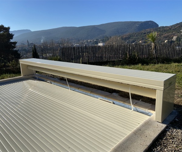 Volet de piscine hors sol en forme de banc de couleur sable, en position fermée sur la piscine, photographié en pleine journée avec un paysage en arrière-plan à Alès.