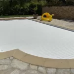 Volet de piscine immergé sur mesure avec lames blanches, en position fermée sur une piscine à Nîmes, photographié en journée.