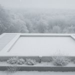 Volet de piscine immergé recouvert de neige, en position fermée sur une piscine en hiver en Ardèche, photographié en journée.